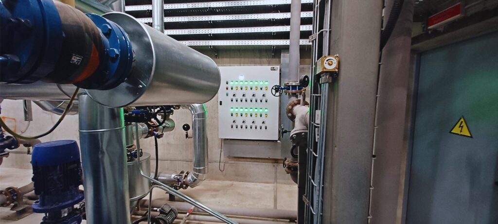 Industrial power plant control system with control panel, pumps, and pipelines inside an engine room